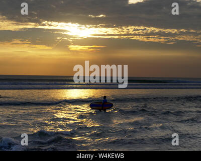 Longboard surfer passeggiate fuori per fare surf al tramonto sulla spiaggia di kuta beach, Bali Foto Stock