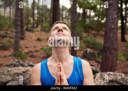 Uomo che guarda verso il cielo e di pregare in una foresta Foto Stock