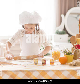 Carino bambina in forma di chef prepara piatti deliziosi in cucina e stendere la pasta con un mattarello Foto Stock