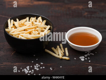 Sale e aceto bastoncini di patate in bianco ciotola, classico snack con ketchup sul legno. Foto Stock