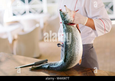 Lo Chef mantenere il salmone. Lo chef taglia il salmone sul tavolo. Foto Stock