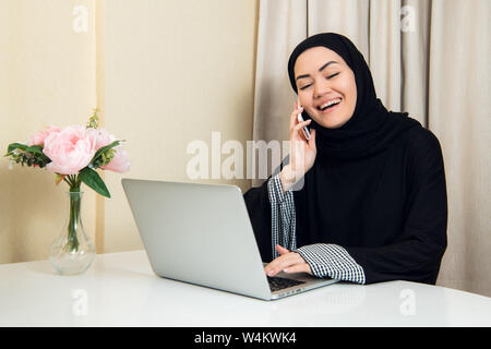 Musulmani lavoratore di sesso femminile a parlare al telefono mentre si lavora con il computer portatile Foto Stock