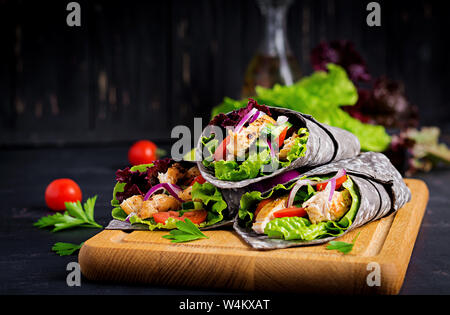 Tortilla con inchiostro aggiunto seppie si avvolge con pollo e verdure su sfondo nero. Burrito di pollo, cibo messicano. Foto Stock