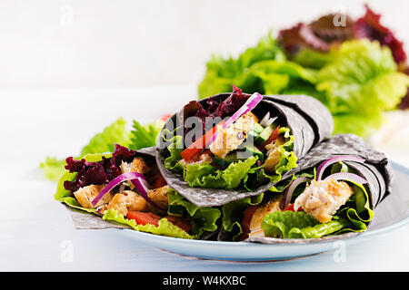 Tortilla con inchiostro aggiunto seppie si avvolge con pollo e verdure su sfondo bianco. Burrito di pollo, cibo messicano. Foto Stock