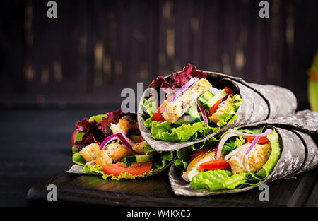 Tortilla con inchiostro aggiunto seppie si avvolge con pollo e verdure su sfondo nero. Burrito di pollo, cibo messicano. Foto Stock