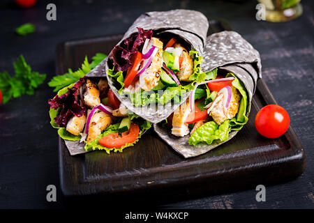 Tortilla con inchiostro aggiunto seppie si avvolge con pollo e verdure su sfondo nero. Burrito di pollo, cibo messicano. Foto Stock