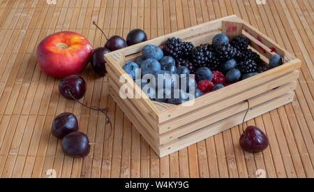 Vita tranquilla con frutte. Lamponi, ciliegie, mirtilli, more e pesche noci piatto. In una piccola cassa di un tappetino. Foto Stock