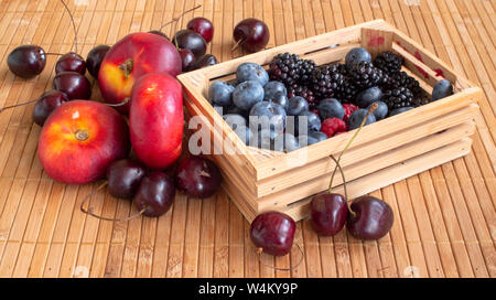 Vita tranquilla con frutte. Lamponi, ciliegie, mirtilli, more e pesche noci piatto. In una piccola cassa di un tappetino. Foto Stock