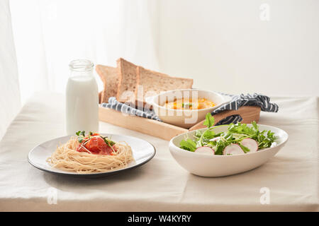 Tavolo per la colazione; spaghetti servito con rafano e insalata con purea di zucca, pane, latte sul tavolo Foto Stock