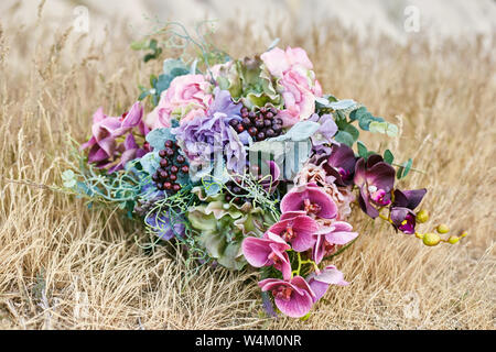 Donna con un bel bouquet di fiori nelle sue mani si erge sulla montagna in raggi dell'alba al tramonto. Bella bianca lunga veste sulla ragazza b Foto Stock