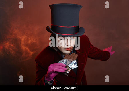 Favoloso circus uomo in un cappello e un abito rosso in posa il fumo su un colore di sfondo scuro. Un clown in un party, uomo gentleman da una fiaba. Wiz Foto Stock