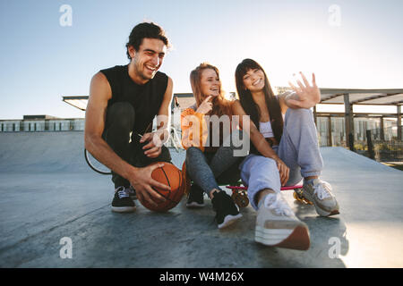 Gruppo di un uomo e di una donna di trascorrere del tempo insieme a skate park. Giovane uomo e donna seduta a skate park e sorridente. Foto Stock