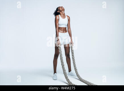 Giovane donna facendo forza di formazione utilizzando corde di battaglia su sfondo bianco. Atleta prendendo una pausa da un intenso allenamento. Foto Stock