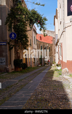 Donna italiana sta in piedi in una scenic marciapiede street tra due fila di case e un tattoo shop di Alghero Foto Stock