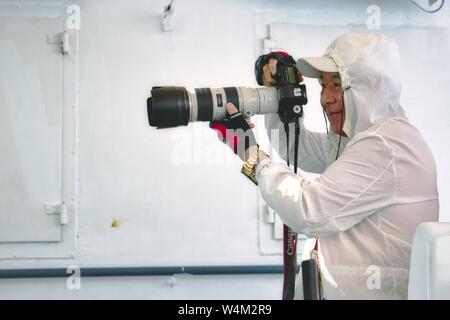 Gozo / Malta - 28 Giugno 2019: un uomo giapponese di scattare una foto a bordo del Gozo/Malta traghetto con un professionista Canon long-range telecamera Foto Stock