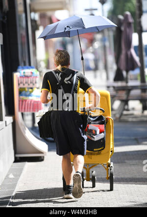 24 luglio 2019, Assia, Frankfurt/Main: sotto un ombrello montato sul suo furgone, gestore di posta Erwin Desch protegge da se stesso le somme a caldo mentre la consegna di posta in abiti estivi in Bornheim distretto. La Germania si trova di fronte a un'ondata di calore - e già mercoledì questo sarà chiaramente evidente in molti settori. Foto: Arne Dedert/dpa Foto Stock
