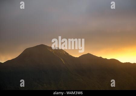 Bella foto ampia di montagne rocciose e colline al tramonto con nuvole grigie e luce solare sul lato Foto Stock