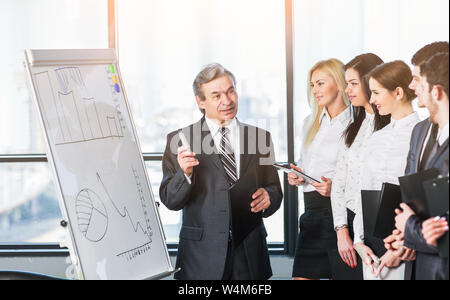 Capo del team aziendale spiega ai suoi colleghi i metodi di crescita delle vendite, utilizzando un supporto di diagrammi e grafici in un ufficio moderno Foto Stock