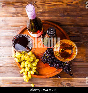 Foto sulla parte superiore del bicchiere di vino al vino con uve nere e verdi sul vassoio in legno su tavola Foto Stock