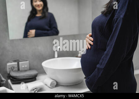 Asian giovani madri vedere uno specchio in bagno Foto Stock