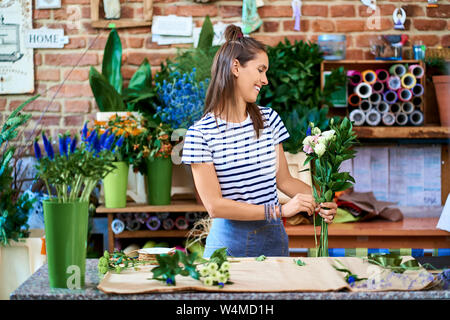 Foto di sorridere un fioraio mettendo insieme dei fiori per un bouquet Foto Stock