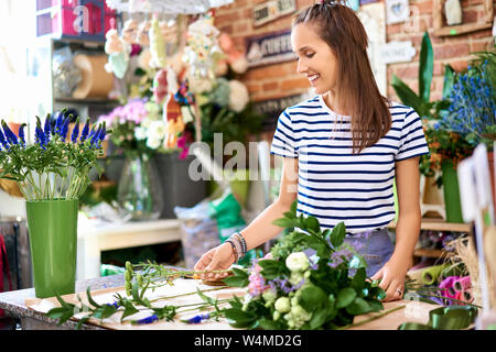 Giovani sorridente fioraio azienda bouquet di fiori e di aggiungere elementi decorativi Foto Stock