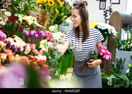 Allegro fiorista giovani al lavoro. La donna la raccolta dei fiori per bouquet Foto Stock