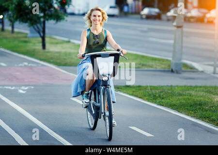 Foto del giovane biondo nella lunga gonna jeans seduti sulla bici su strada in città sul giorno di estate Foto Stock