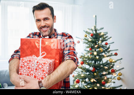 Ritratto di uomo sorridente tenendo i regali di Natale in sala decorata e guardando la fotocamera Foto Stock