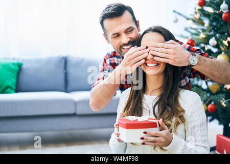 Uomo che copre la fidanzata agli occhi e sorprendente con il suo regalo di natale Foto Stock