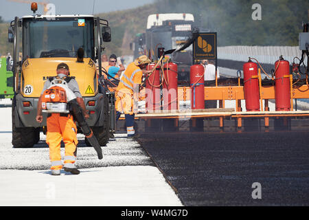 24 luglio 2019, Renania-Palatinato, Zeltingen-Rachtig: i lavoratori asfalto la superficie stradale del ponte Hochmosel in costruzione a temperature ben al di sopra di 30 gradi Celsius. Non vi è alcun luogo ombroso su 160 metri di un edificio alto sopra la valle di Mosel. Foto: Thomas Frey/dpa Foto Stock