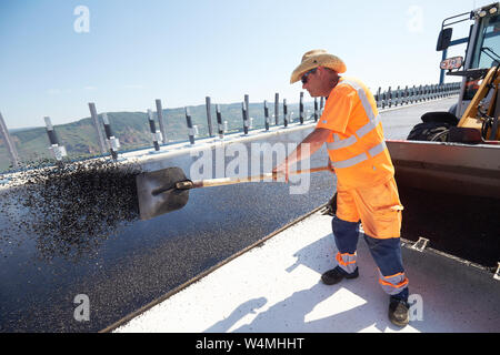 Rachtig Zeltingen, Germania. Il 24 luglio, 2019. Lavoratori asfalto la superficie stradale del ponte Hochmosel in costruzione a temperature ben al di sopra di 30 gradi Celsius. Non vi è alcun luogo ombroso su 160 metri di un edificio alto sopra la valle di Mosel. Credito: Thomas Frey/dpa/Alamy Live News Foto Stock