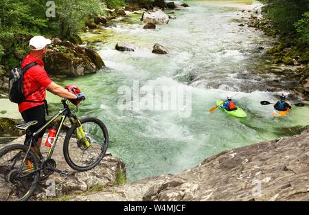 Un uomo con una mountainbike guarda rematori nelle loro canoe in azione sul fiume Soca vicino a Bovec in Slovenia sulla luglio 09, 2019. Foto: Wolfram Steinberg/dpa | Utilizzo di tutto il mondo Foto Stock