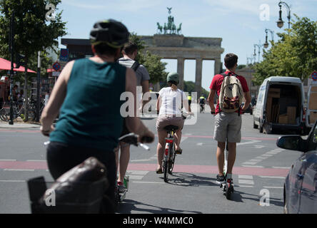 Berlino, Germania. Il 24 luglio, 2019. E-scooter e i ciclisti si incontrano in un semaforo rosso davanti alla Porta di Brandeburgo. Credito: Jörg Carstensen/dpa/Alamy Live News Foto Stock