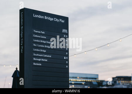 London, Regno Unito - 22 Giugno 2019: segnaletica direzionale da London Bridge al porticciolo della città al tramonto, contro il cielo, il fuoco selettivo. Il molo serve come il molo principale per t Foto Stock