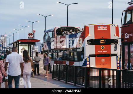 London, Regno Unito - 22 Giugno 2019: la gente camminare passato l'originale tour bus dipinta come Unione Jack parcheggiata vicino al London Bridge, la sera. Londra è uno o Foto Stock