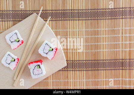 Quattro bobine con polpa di granchio e il cetriolo con la Flying Fish roe. Su un supporto di legno con bacchette.Foie rug per rotoli. Foto Stock