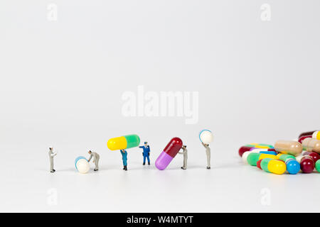 Mucchio di pillole di medicina con la gente in miniatura su sfondo bianco Foto Stock