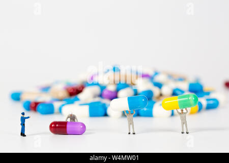 Mucchio di pillole di medicina con la gente in miniatura su sfondo bianco Foto Stock