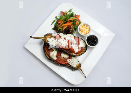 Un basso contrasto eroe caldo colpo di un corso principale piatto con melanzane grigliate con mozzarella di bufala, pomodori, olive e verdure sul lato su un minim Foto Stock