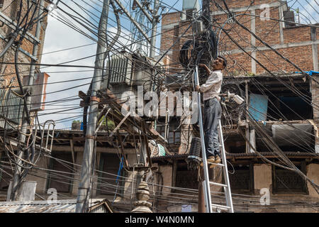 Tecnico su una scala Controllo di cavi in Kathmandu Foto Stock