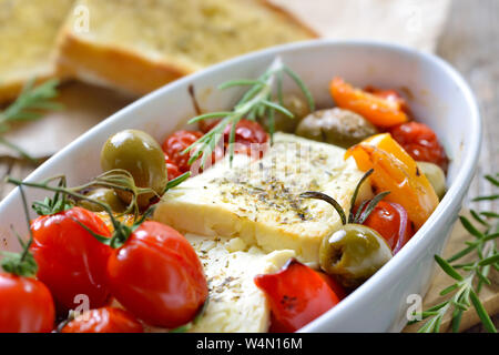 Caldo antipasto greco: cotto il formaggio feta con olive verdi, pomodori ciliegini, peperoni, cipolle e olio d'oliva servito con arrosti di herb baguette Foto Stock