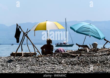 24 luglio 2019, Baden-Wuerttemberg, Gohren am Bodensee: due donne siedono sulla riva del lago di Costanza sotto gli ombrelloni, mentre una barca in background. Foto: Felix Kästle/dpa Foto Stock