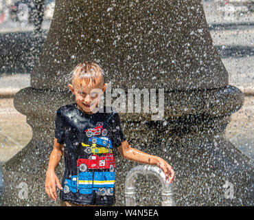 24 luglio 2019, Assia, Frankfurt/Main: sei-anno-vecchio Artem sorge nell'estate calore sotto la fontana presso la Alte Oper e viene irrorato off dall'acqua fredda. Foto: Frank Rumpenhorst/dpa Foto Stock
