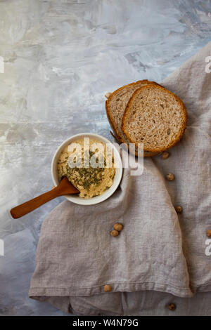 Deliziosa pasta di ceci con diverse erbe con sfornato fresco e fette di pane di grano su sfondo grigio. Foto Stock