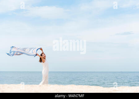 Donna sulla spiaggia, Ritratto di giovane donna felice indossando abito bianco e la holding scraft tropicale sulla spiaggia di sabbia. Concetto di estate.