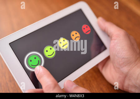 Uomo a fornire una valutazione su un dispositivo elettronico su un tavolo di legno. Composizione orizzontale. Vista in elevazione. Foto Stock