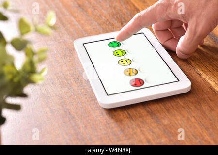 Uomo a fornire una valutazione su un dispositivo elettronico su un tavolo di legno. Composizione orizzontale. Vista in elevazione. Foto Stock