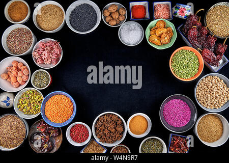 Su uno sfondo nero ciotole piene di specie secchi e legumi Hibiscus, giallo lenticchie, lenticchie verdi, rosa arooz, anice stellato, ceci, sesamo, oat Foto Stock