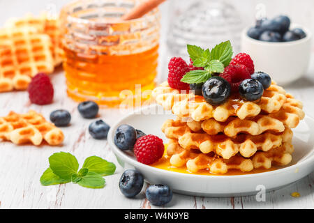 Viennese cialde croccanti con frutti di bosco freschi (lamponi e mirtilli) con il miele e le foglie di menta su una piastra bianca sul tavolo. Deliziosa casa Foto Stock